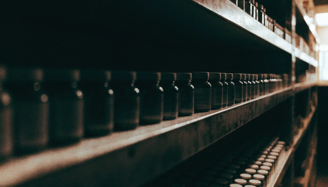 An out-of-focus row of plain supplement bottles on a pharmacy back-room shelf with deep shadows